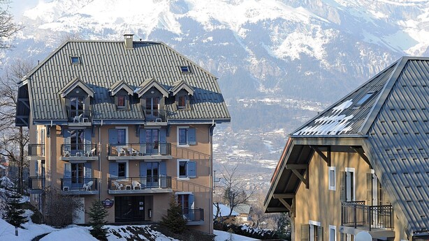 A multi-story hotel with balconies and a mountain backdrop.