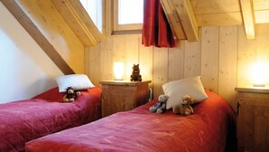 A cozy bedroom with two beds, wooden walls, and a sloped ceiling.