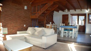 A cozy living room with a white sofa, a dining table with chairs, and a kitchen area visible in the background. - Near Delmar (house 2) (Mar Azul)