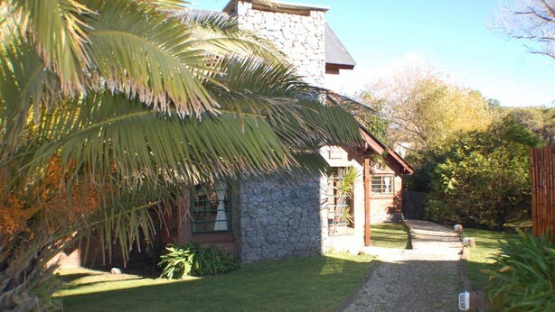 A stone house with a thatched roof, surrounded by a well-maintained garden and a palm tree. - Near Delmar (house 2) (Mar Azul)
