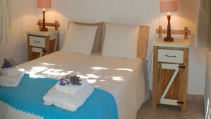 A bedroom with a wooden ceiling, a bed with a blue and white bedspread, two bedside tables with lamps, and a wall with three framed pictures. - Near Delmar (house 2) (Mar Azul)