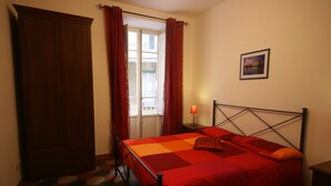 A bedroom with a bed, a wardrobe, a window with curtains, a nightstand with a lamp, and a framed picture on the wall. - apartment In the heart of Rome wonderful view front of the Colosseum discounts (Roma)