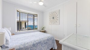 Ein Schlafzimmer mit einem Bett, einem Babybett, einem Fenster mit Jalousien, einem Deckenventilator und einem an der Wand hängenden Kunstwerk.
