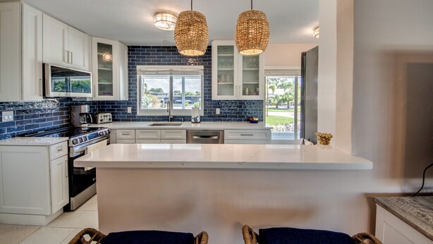 A modern kitchen with white cabinets, a large island, and a view of the outdoors. - West Facing Elec Heated Pool, 2024 Tritoon rental, Walk/Bike to Bars&Restaurants (Cape Coral)
