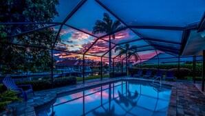 A pool area with a glass enclosure, lounge chairs, and a sunset view. - West Facing Elec Heated Pool, 2024 Tritoon rental, Walk/Bike to Bars&Restaurants (Cape Coral)