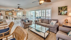 A spacious living room with a glass coffee table, two sofas, wicker chairs, and ceiling fans. - West Facing Elec Heated Pool, 2024 Tritoon rental, Walk/Bike to Bars&Restaurants (Cape Coral)