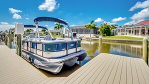 A boat docked at a pier with a clear view of the water and a covered area with chairs. - West Facing Elec Heated Pool, 2024 Tritoon rental, Walk/Bike to Bars&Restaurants (Cape Coral)