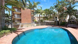 A swimming pool surrounded by palm trees and a brick building. - Kookaburra Court Unit 1 Bulcock Beach QLD (CALOUNDRA)