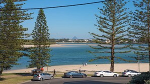 A coastal view with a beach, parked cars, and a clear sky. - Kookaburra Court Unit 1 Bulcock Beach QLD (CALOUNDRA)