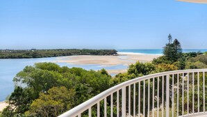 Une vue sur la côte depuis un balcon doté d’une balustrade, donnant sur une plage aux eaux d’un bleu limpide et au rivage sablonneux.