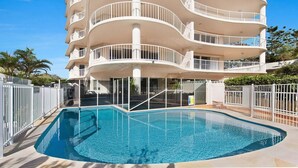 Un immeuble à plusieurs étages avec une piscine devant.