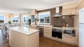 Une cuisine moderne dotée d’un îlot central, d’appareils électroménagers en acier inoxydable et offrant une vue sur la mer.