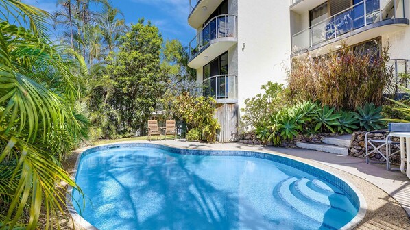 A swimming pool surrounded by lush greenery and a multi-story building with balconies. - Blue Horizon Unit 1 Bulcock Beach QLD (CALOUNDRA)