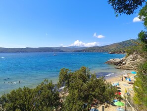 Una playa costera con agua azul cristalina, una orilla arenosa y un promontorio rocoso.