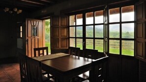 A dining area with a wooden table and chairs, large windows with a view of greenery, and a door leading outside.