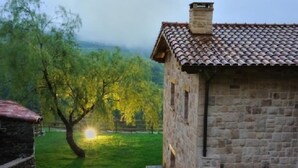 A stone building with a tiled roof, surrounded by a grassy area and trees.