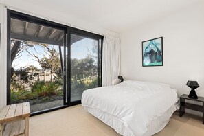 A bedroom with a large sliding glass door leading to an outdoor area, a bed with white bedding, a small bedside table with a lamp, and a framed picture on the wall. - Treetops Terrace 10 at C-Air (Skenes Creek, Apollo Bay)