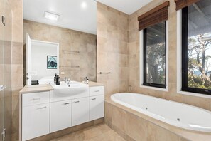 A modern bathroom with a freestanding bathtub, a large mirror, and a window with a view of trees. - Treetops Terrace 10 at C-Air (Skenes Creek, Apollo Bay)