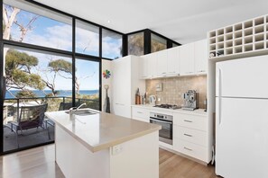 Uma cozinha moderna com uma ilha grande, forno embutido e vista para o mar.