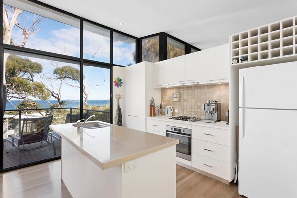 A modern kitchen with a large island, a built-in oven, and a view of the sea.