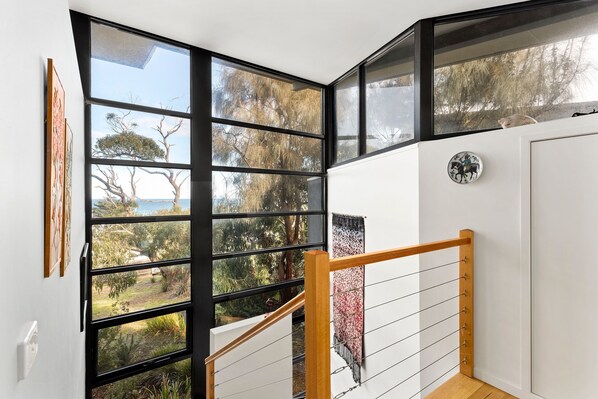A corner room with large windows, a wooden staircase, and a wall-mounted plate with a horse design.
