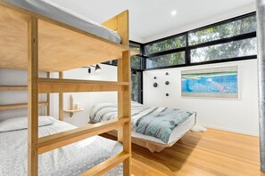 A bunk bed room with a view of trees through large windows, a painting on the wall, and a shelf with items.