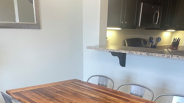 A dining table with four chairs, a kitchen area with a microwave and utensils, and a mirror on the wall. - Beautiful Rehoboth Beach Condo! 3 bed 2 bath! 2 Pools! Tennis! Gym!  (Rehoboth Beach)