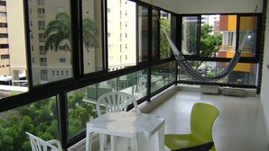 A balcony with a table and chairs, a hammock, and a view of buildings and trees. - Affordable option in pleasant accommodation near the beach (Electricity included). (Fortaleza)