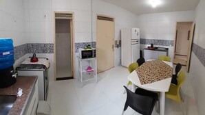 A compact kitchen with a microwave, kettle, and refrigerator. There is a dining table with chairs and a water dispenser. - Affordable option in pleasant accommodation near the beach (Electricity included). (Fortaleza)