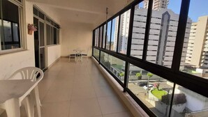 A balcony with a view of tall buildings, a small table, and two chairs. - Affordable option in pleasant accommodation near the beach (Electricity included). (Fortaleza)