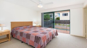 A bedroom with a bed, a nightstand, a lamp, a ceiling fan, and a sliding glass door to the outside.