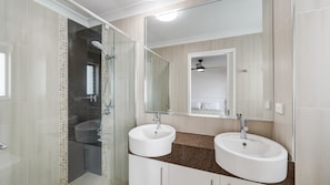Une salle de bain avec deux lavabos, une douche et un miroir.