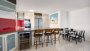 Una cocina moderna con encimera roja, electrodomésticos integrados y una zona de comedor con sillas de madera y una mesa blanca.