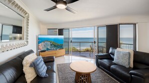 A living room with a TV, two leather sofas, a coffee table, and a balcony with a view of the ocean. - Pandanus Shores Unit 9 Kings Beach QLD (KINGS BEACH)