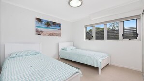 Ein Schlafzimmer mit zwei Betten, einem Wandbild im Strandstil und einem Fenster mit Blick auf Bäume.