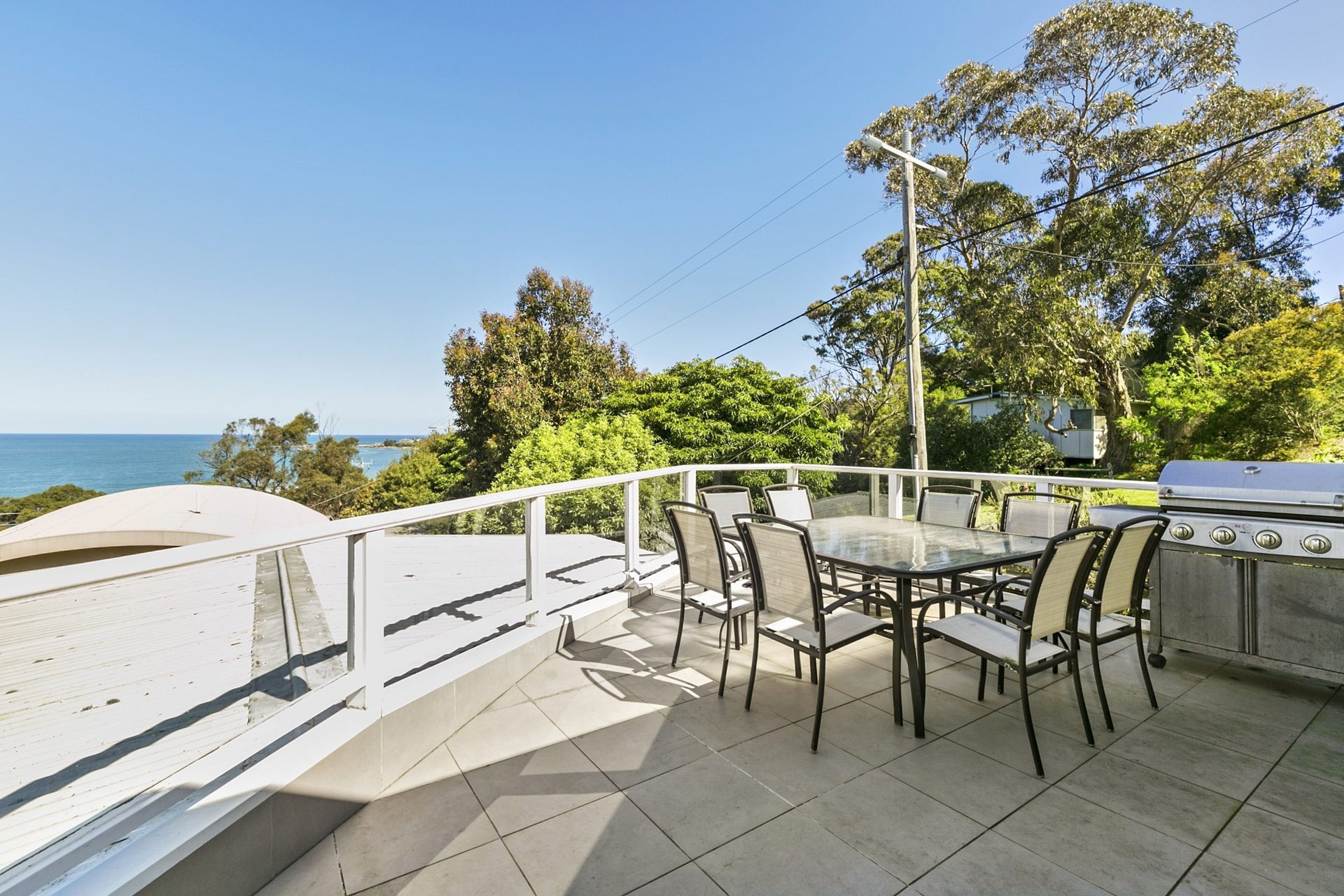 An outdoor patio with a table and chairs, a grill, and a view of the sea.