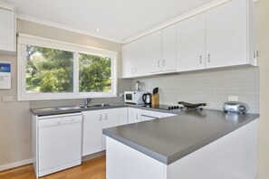 A modern kitchen with white cabinetry, a built-in microwave, and a large window overlooking greenery. - Christoe (Lorne)