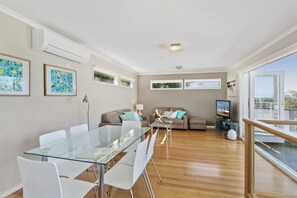 Een moderne woonkamer met een glazen eettafel, witte stoelen, een bank en een televisie.