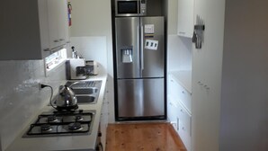 A compact kitchen with a gas stove, microwave, refrigerator, and wooden floor.