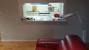 A living room with a red leather sofa, a kitchen area with a window, and a mounted desk with a lamp.