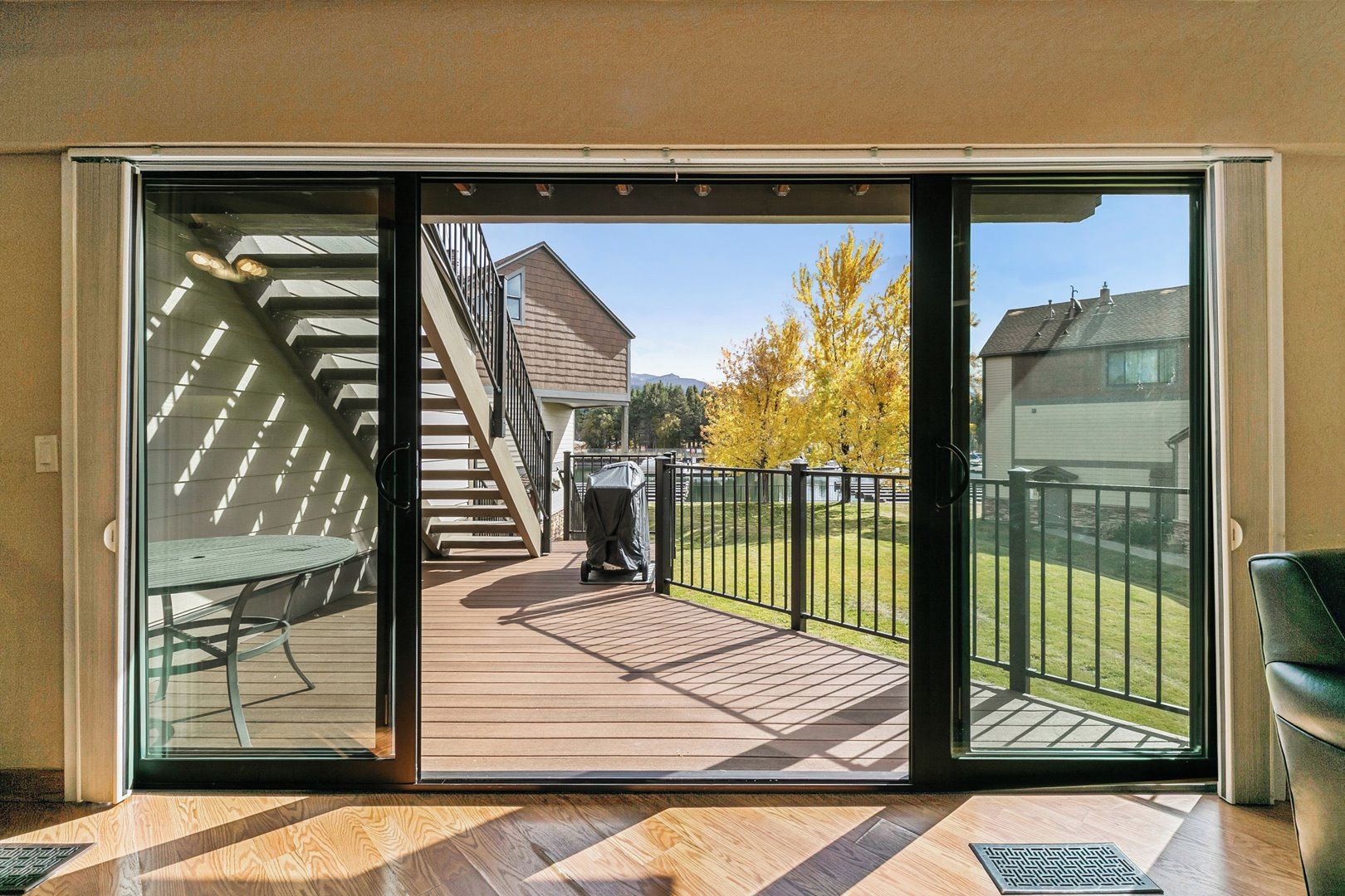 Une porte-fenêtre coulissante donne sur une terrasse extérieure équipée d’un barbecue couvert, d’un escalier et offrant une vue sur un quartier résidentiel.