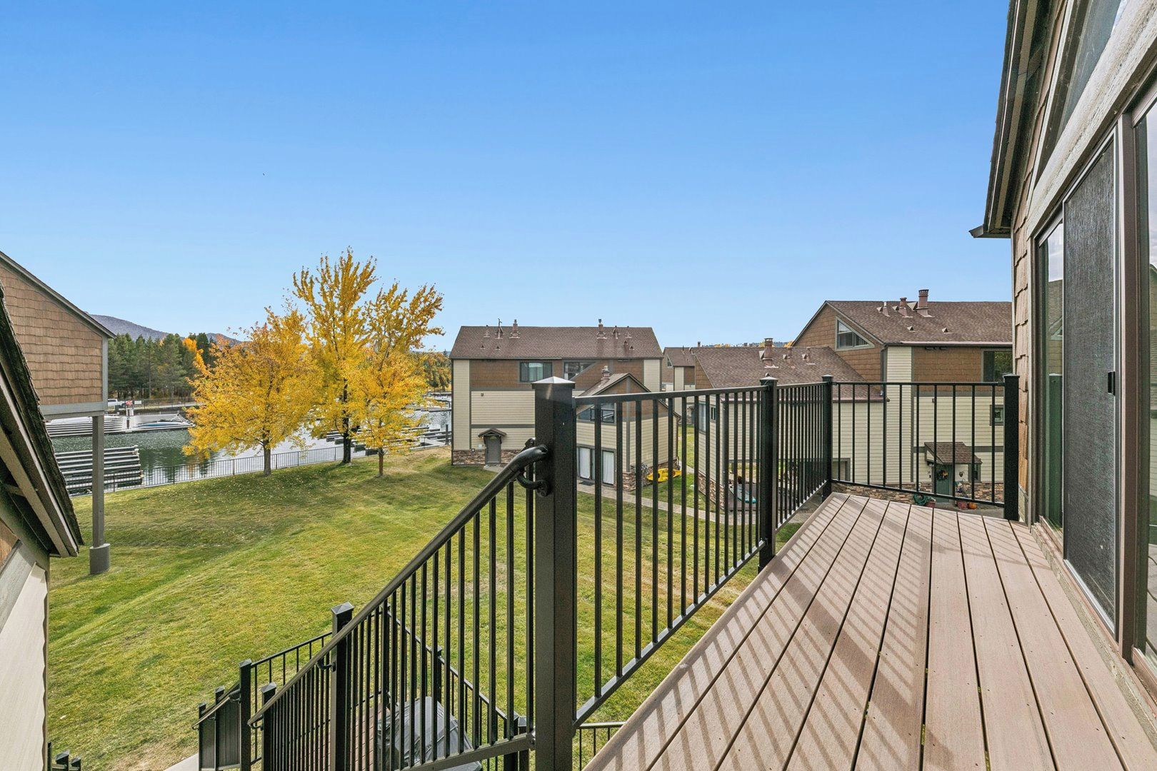 Un barrio residencial con una terraza de madera, una cerca de metal y casas al fondo.
