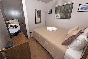 A bedroom with a bed, a mirror, a television, and a window with a poster.