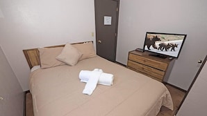 Hotellihuone, jossa on sänky, televisio ja puinen yöpöytä.