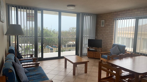Relax in this cozy living area with a sofa set, television, and dining table, plus a balcony with a table and chairs.