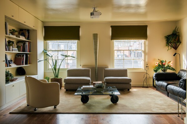 Un salon comprenant un canapé, un fauteuil et une table basse, une bibliothèque et un radiateur.