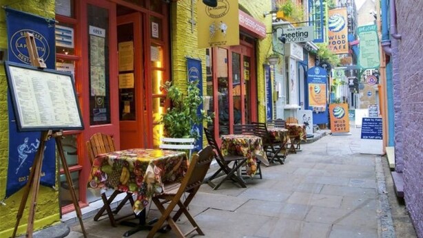 Una calle estrecha con terrazas y varios cafés.