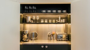 Una cocina compacta con cafetera, tostadora y varios vasos en estantes.