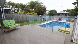 A backyard with a swimming pool, a wooden deck, a fenced area, and a wooden fence.