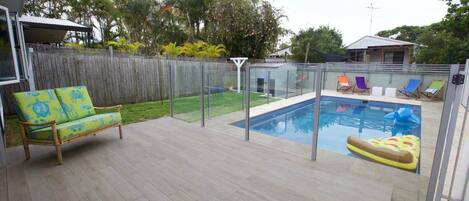 A backyard with a swimming pool, a wooden deck, a fenced area, and a wooden fence.
